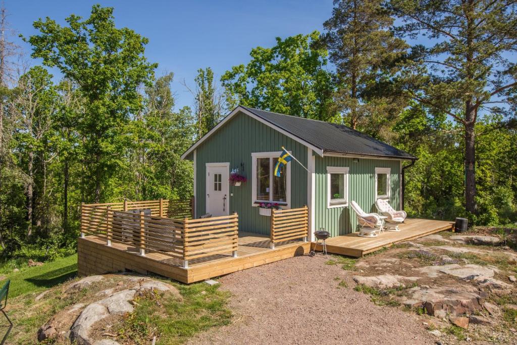 a green tiny house with a porch and a deck at Cozy holiday house close to nature in Ödeshög, Gränna in Ödeshög