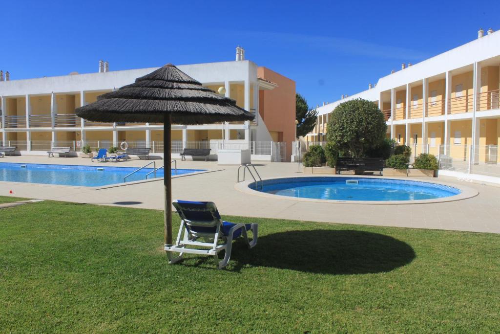 a chair under an umbrella next to a swimming pool at Pool&Beach in Encosta de São José in Albufeira