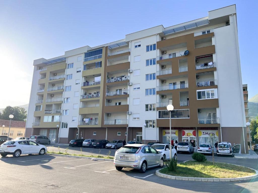 um grande edifício de apartamentos com carros estacionados num parque de estacionamento em Apartman Jelena em Trebinje