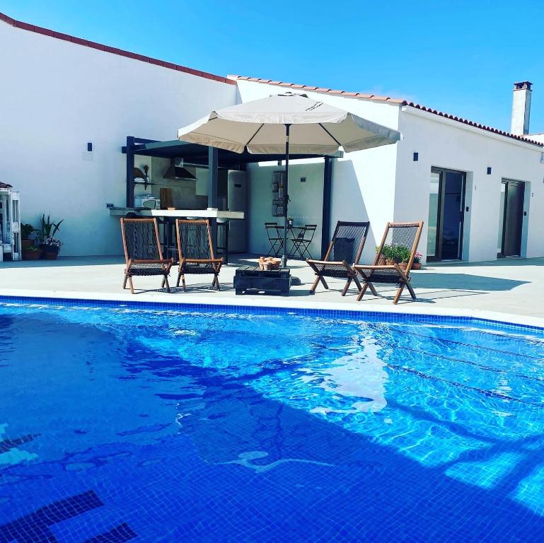 a swimming pool with two chairs and an umbrella at Alojamiento El Miajon de los Castúos in Valdesalor