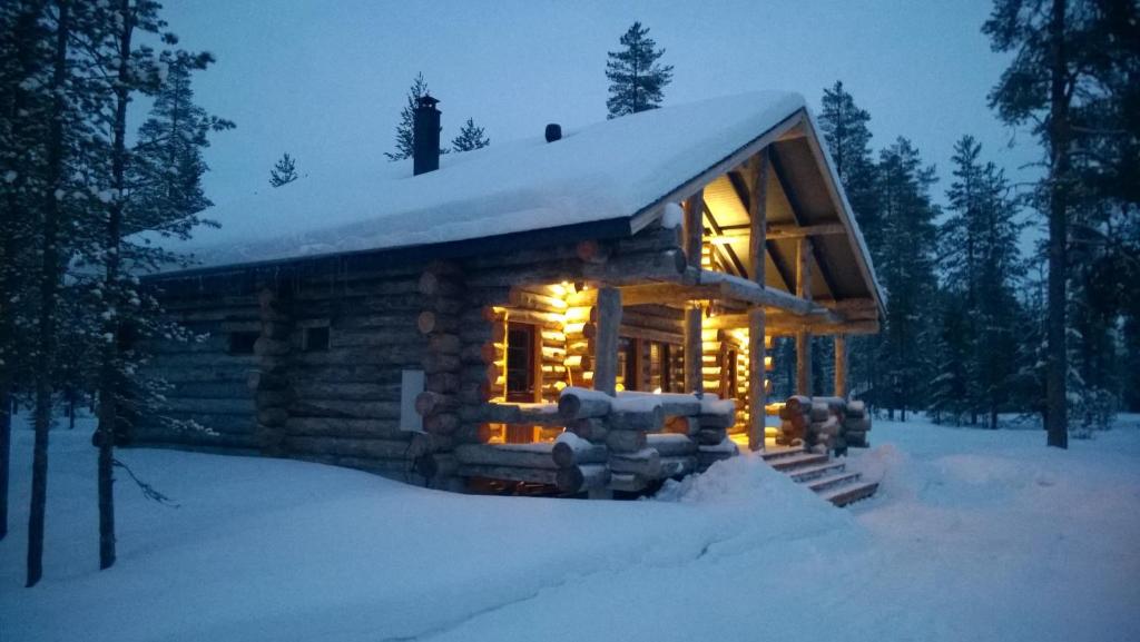 Cabaña de madera con luces encendidas en la nieve en Revontuli Cottage, en Kolari