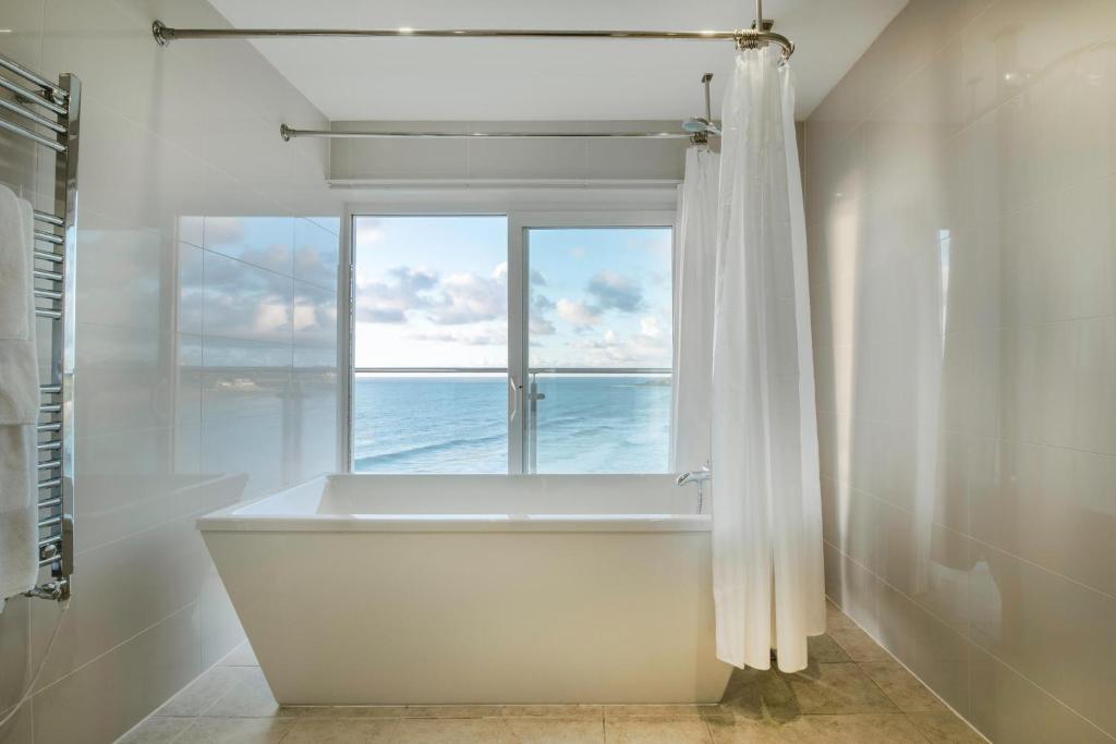 a bathroom with a bath tub and a window at Fistral Beach Hotel and Spa - Adults Only in Newquay