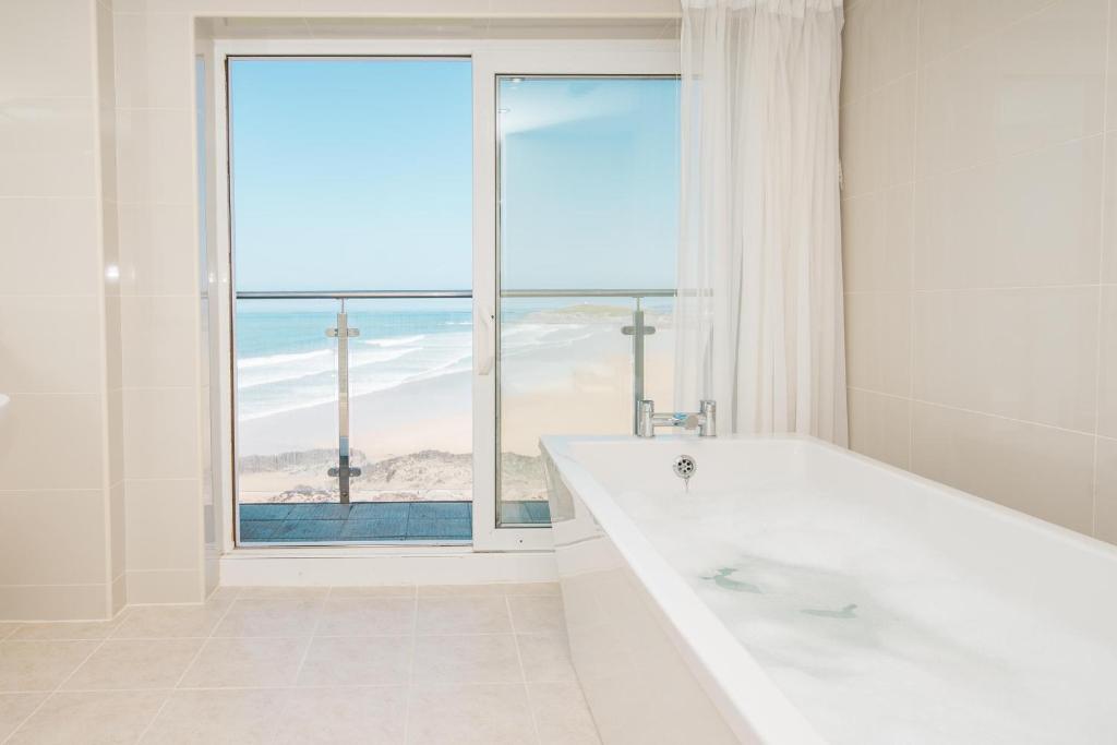 a white bathroom with a large tub and a window at Fistral Beach Hotel and Spa - Adults Only in Newquay