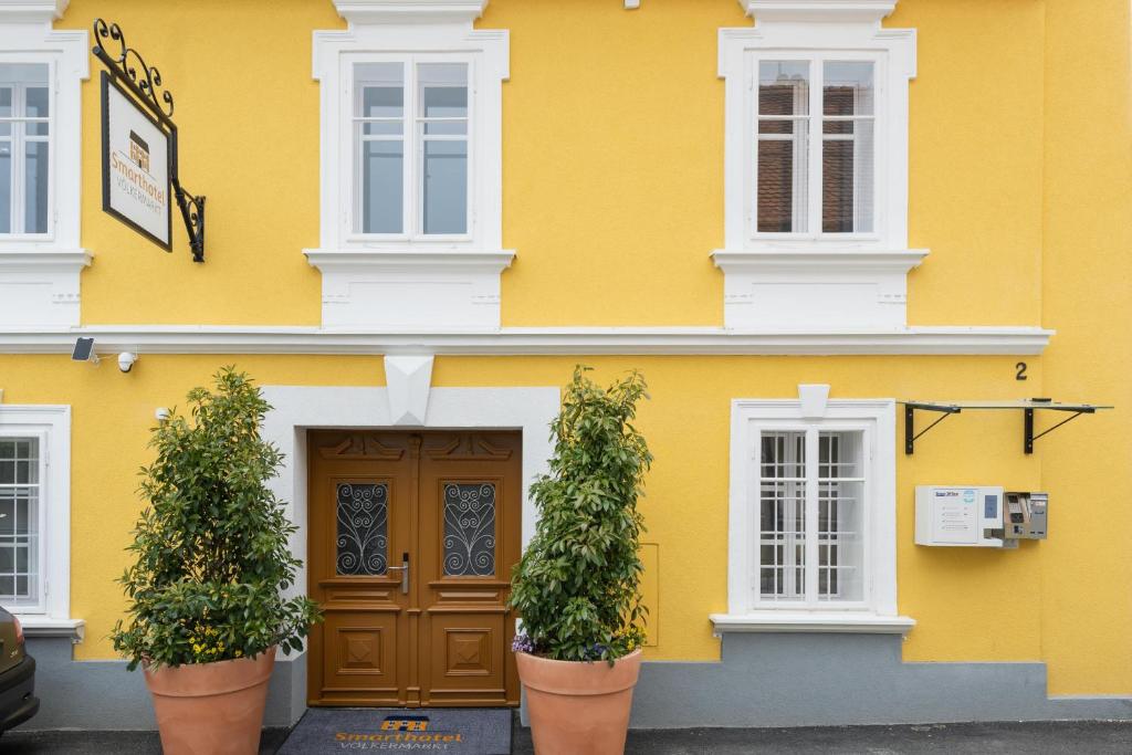 un bâtiment jaune avec deux plantes en pot devant lui dans l'établissement Smarthotel Völkermarkt, à Völkermarkt