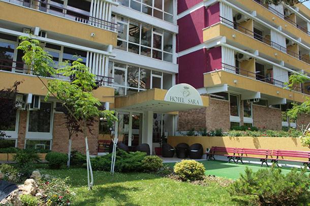 a large apartment building with a bench in front of it at Hotel Sara in Neptun