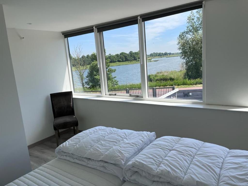 a bedroom with a bed and a chair in front of a window at Comfortabele woning mét omheinde tuin aan water voor 12 p in Oostburg