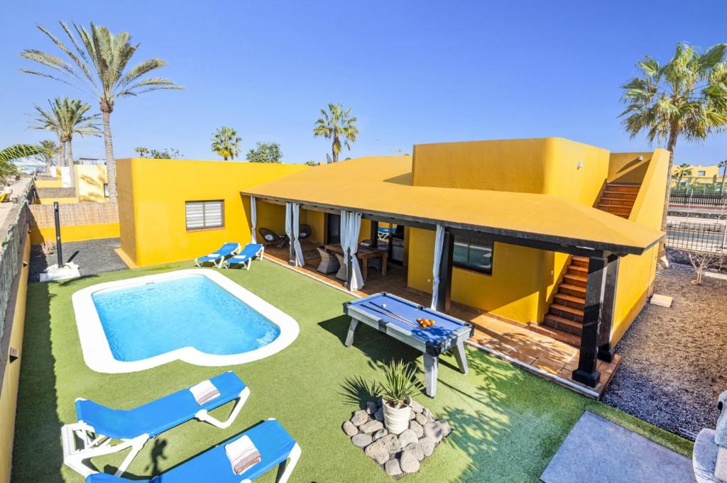 a yellow house with a swimming pool and some chairs at Villa Papagayo Deluxe by Villa Plus in Corralejo