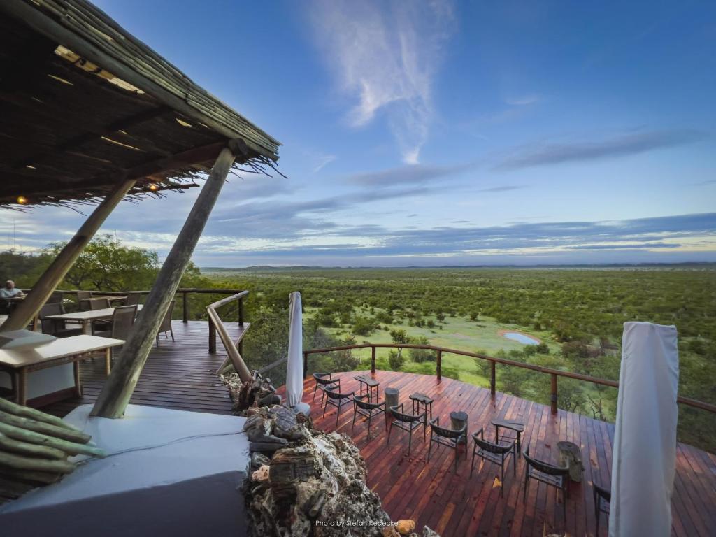 a deck with chairs and tables and a view of a field at Ongava Lodge in Okaukuejo