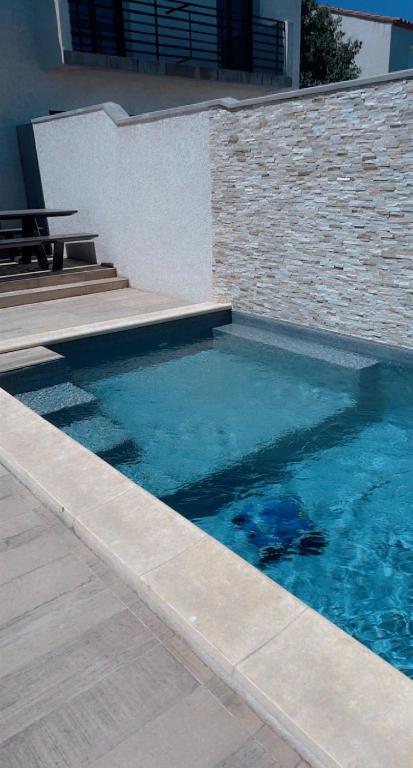 - une piscine d'eau bleue à côté d'un mur de briques dans l'établissement Maison avec Picine, à Perpignan