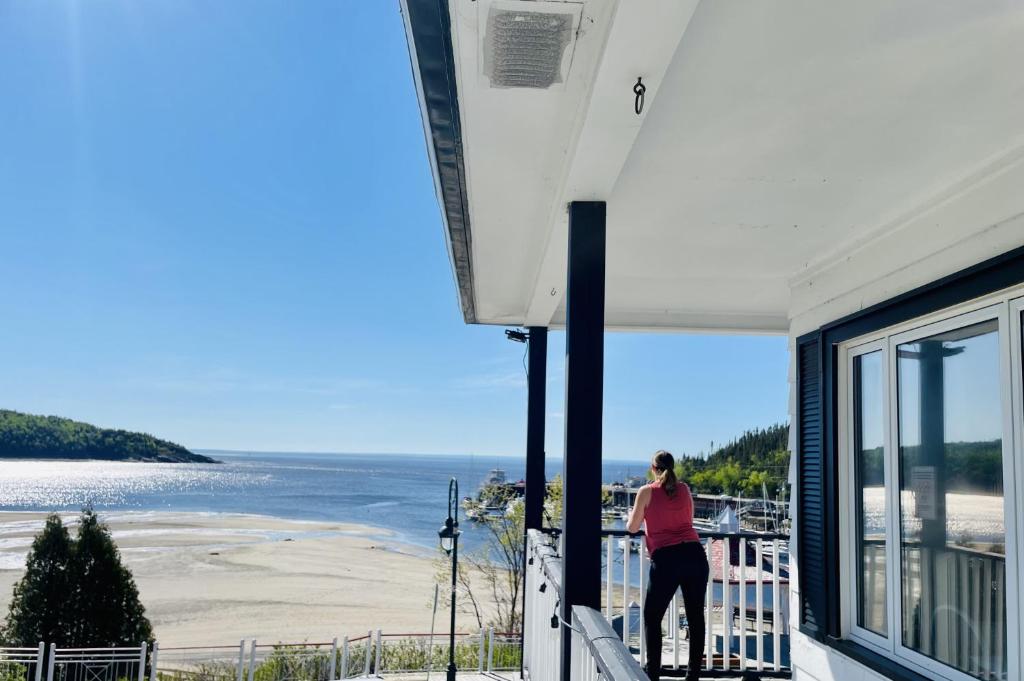 a woman standing on a balcony looking out at the beach at La Merveilleuse - Baie de Tadoussac Vue panoramique in Tadoussac
