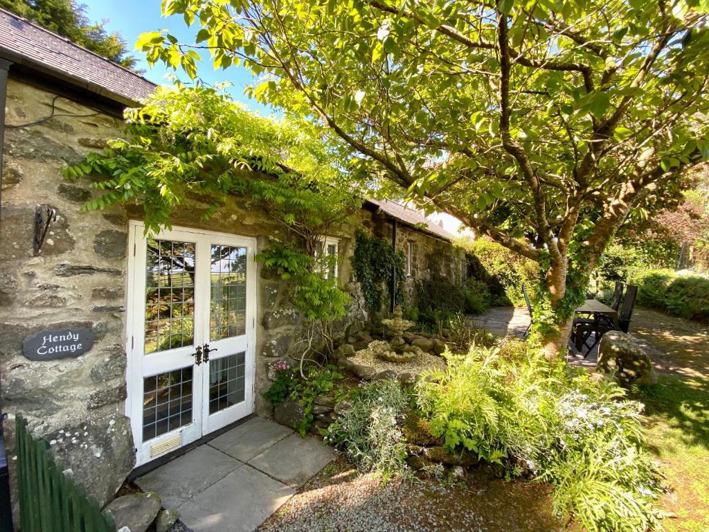 a stone house with a white door and a tree at Hendy Cottage in Pwllheli