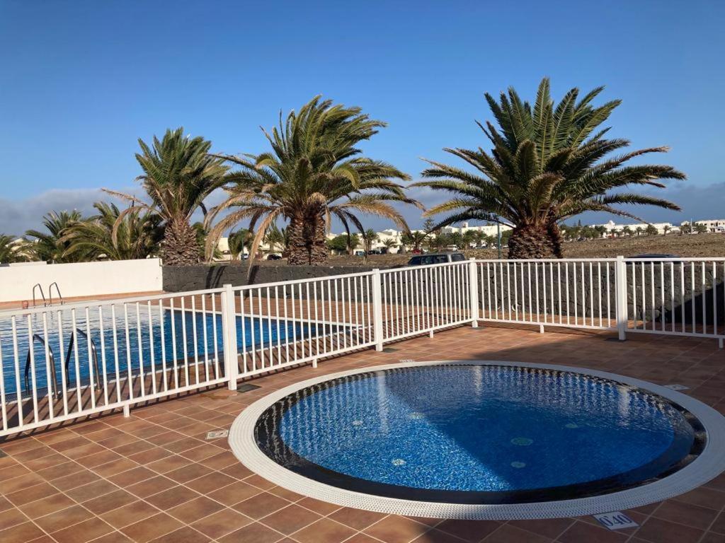 a swimming pool with a white fence and palm trees at Kiltankin beag in Costa Teguise