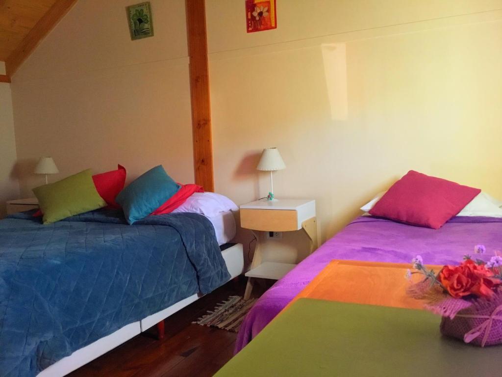 een slaapkamer met 2 bedden met kleurrijke kussens en een tafel bij Los Neneos Chalten in El Chalten