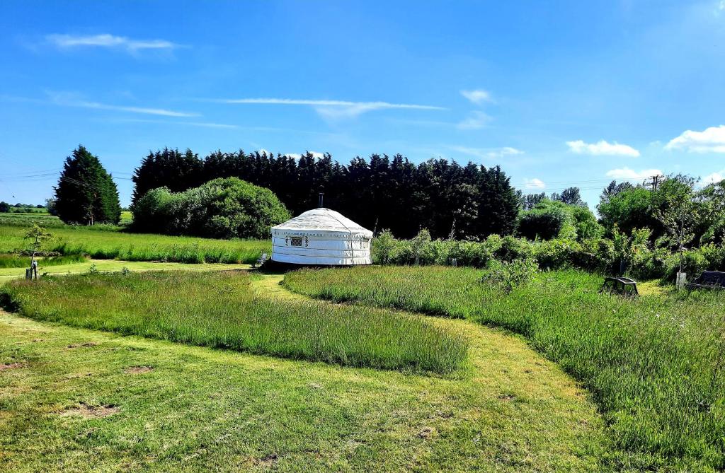a field with a white building in the middle at Cranfield Retreat & Glamping - Yurt & Shepherds Hut in Long Melford