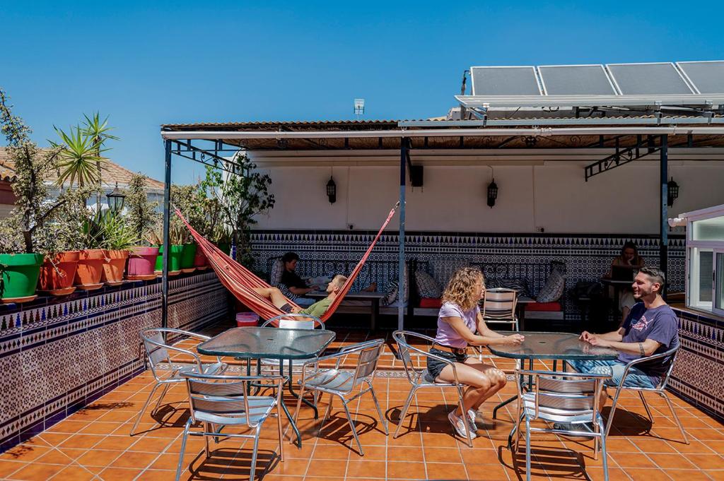 eine Gruppe von Personen, die an Tischen mit Hängematten auf dem Dach sitzen in der Unterkunft Hostel Triana Backpackers in Sevilla