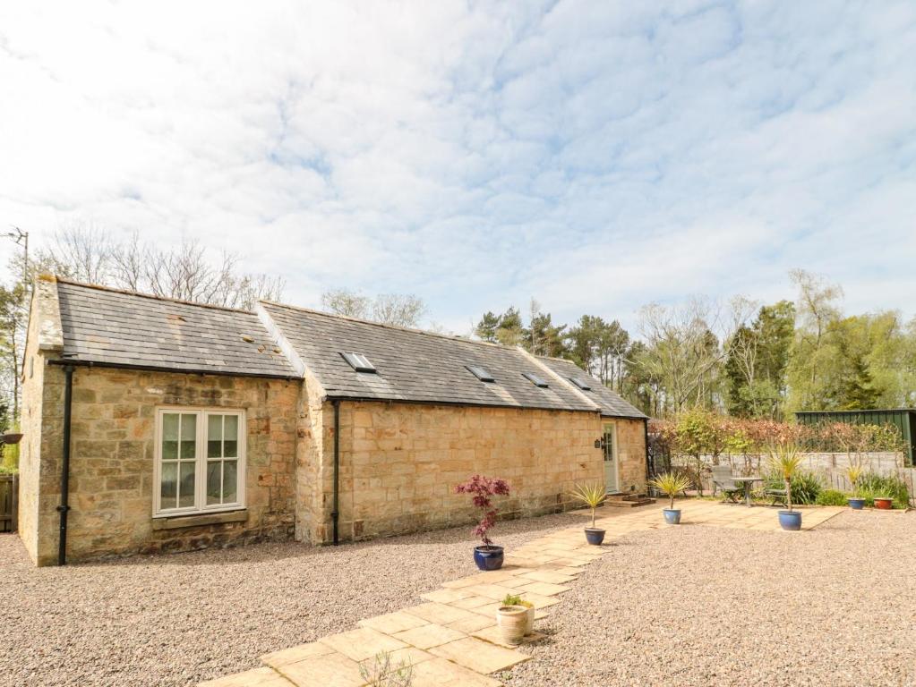 a stone barn with a gravel driveway in front of it at Kizzie Cottage in Morpeth