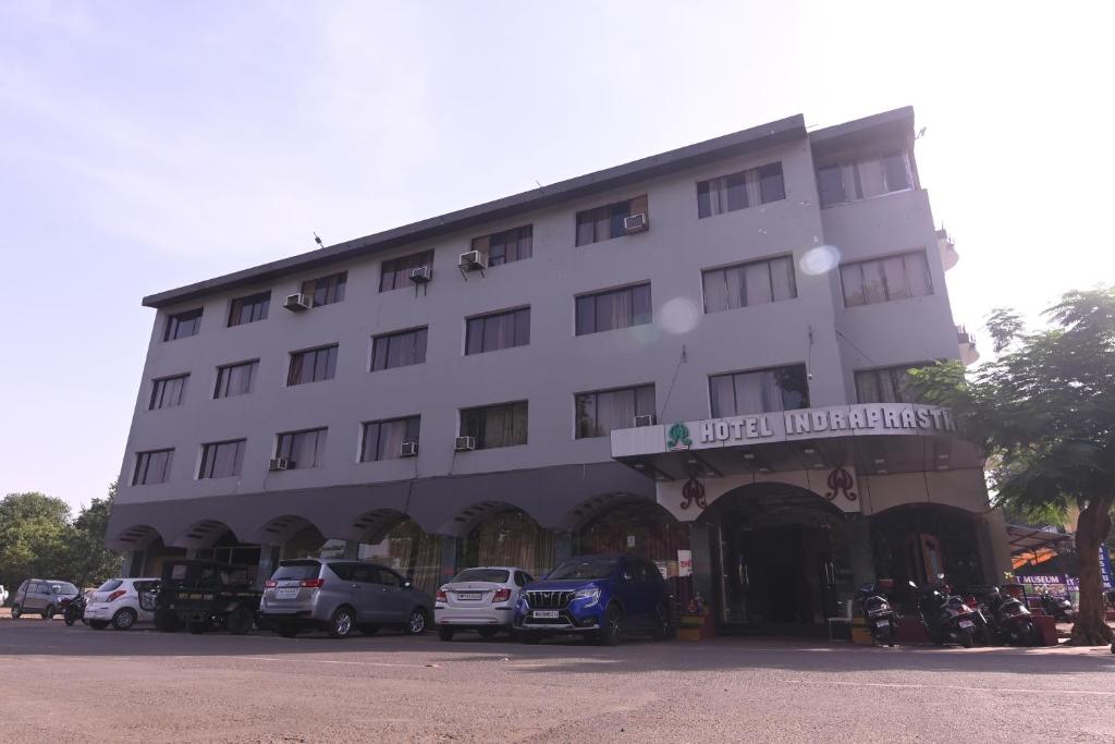 伯杰默里Hotel Indraprastha pachmarhi的一座白色的大建筑,前面有汽车停放