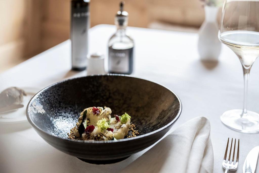 a bowl of food on a table with a wine glass at Adler Spa Resort Dolomiti in Ortisei