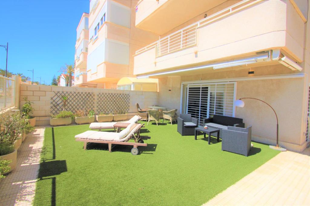 un patio trasero con césped y muebles verdes y un edificio en Apartamento CasaTuris enfrente al mar en Playa Muchavista C102, en El Campello