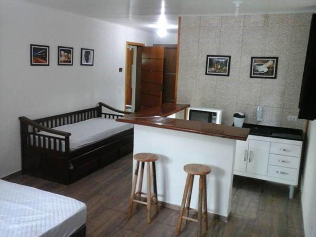 a bedroom with a bed and a kitchen with stools at Refúgio Melissa in Campos do Jordão