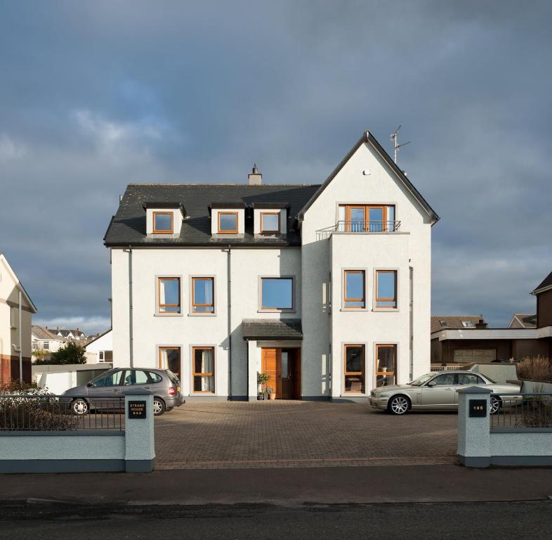 duży biały dom z samochodami zaparkowanymi na parkingu w obiekcie Strand House w mieście Portstewart
