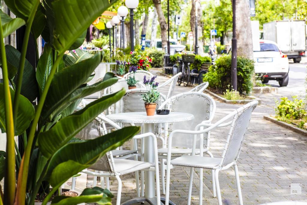 a white table and chairs on a sidewalk with plants at Hotel Fattori Mare in Cesenatico