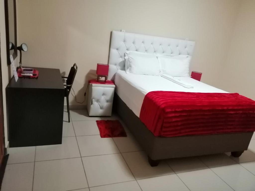 1 dormitorio con 1 cama con manta roja y escritorio en Beautiful Gate Guesthouse, en Palapye