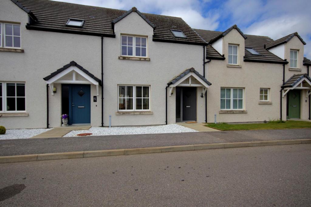 a white house with blue doors on a street at 3 Mackay Road in Dornoch