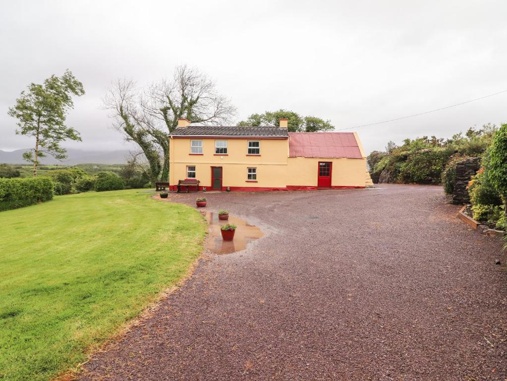 une grande maison jaune avec un toit rouge dans une allée de gravier dans l'établissement Ceol Na N'ean, à Sneem