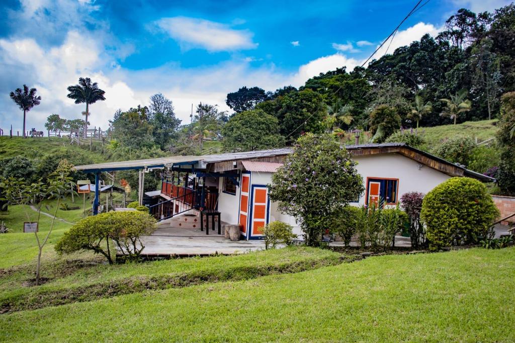 una pequeña casa blanca con puertas naranjas en un campo en Cerro Verde Salento, en Salento