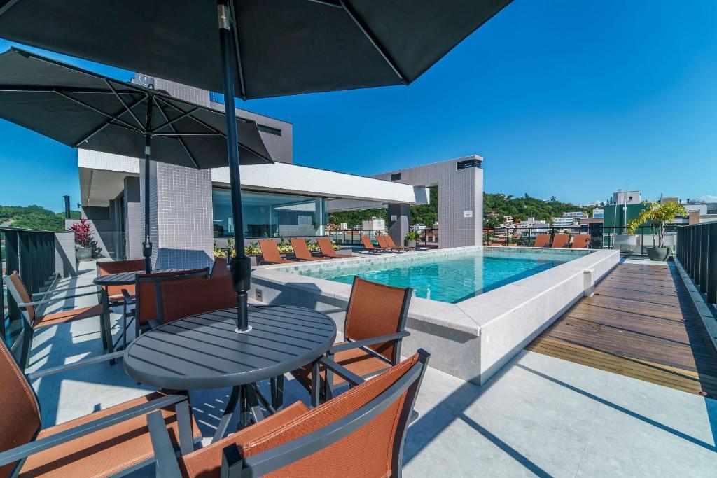 eine Terrasse mit Tisch und Stühlen und ein Swimmingpool in der Unterkunft Adra 206 - Apartamento no centro de Bombinhas - Rooftop com piscina e academia - À poucos metros da praia - (Consultar serviços de roupas de cama e banho) in Bombinhas