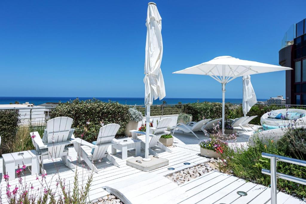 a patio with white chairs and an umbrella and the ocean at Shalom Hotel & Relax - an Atlas Boutique Hotel in Tel Aviv