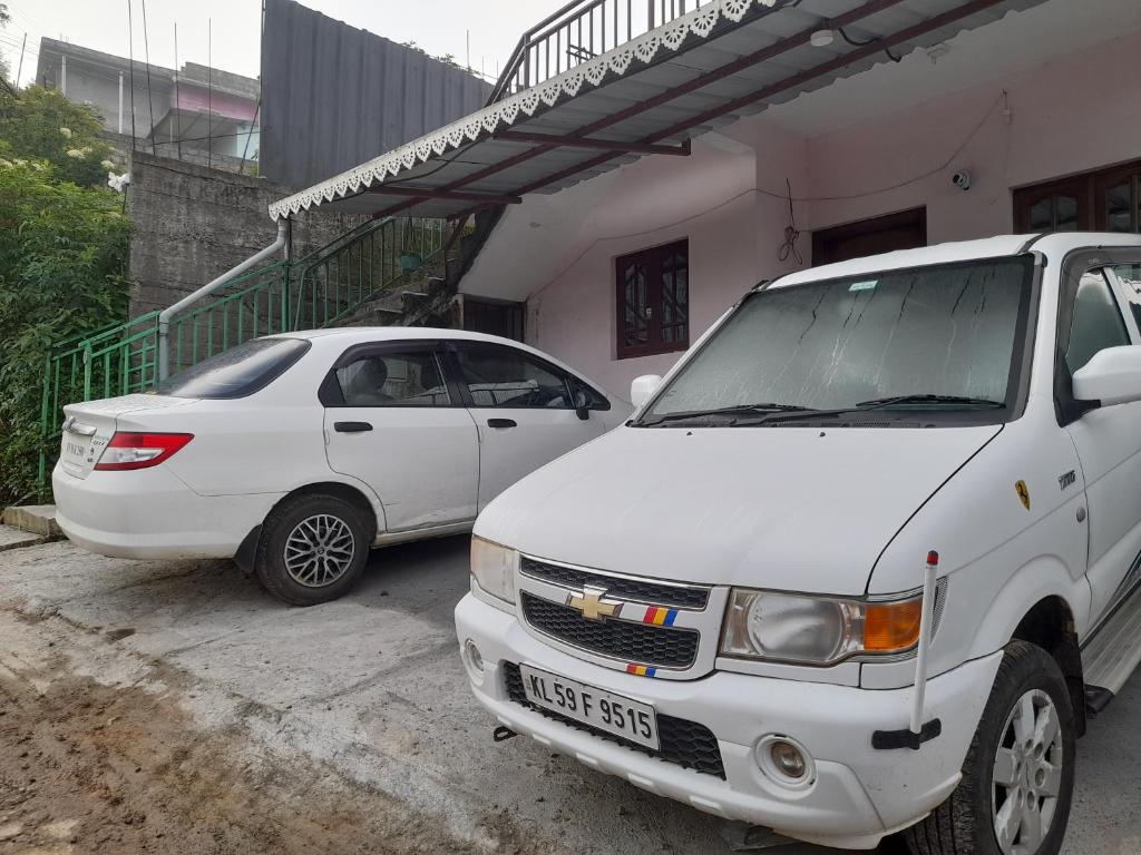 two white cars parked in front of a building at Munnar Brindavan Cottage in Munnar