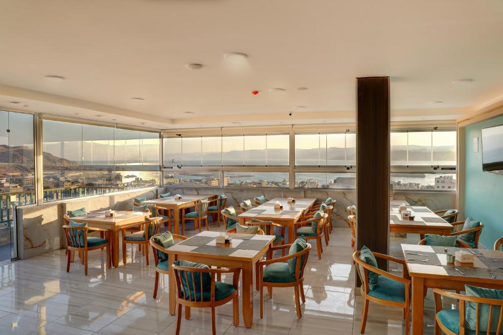 un restaurante con mesas y sillas de madera y ventanas en Turquoise Hotel en Áqaba