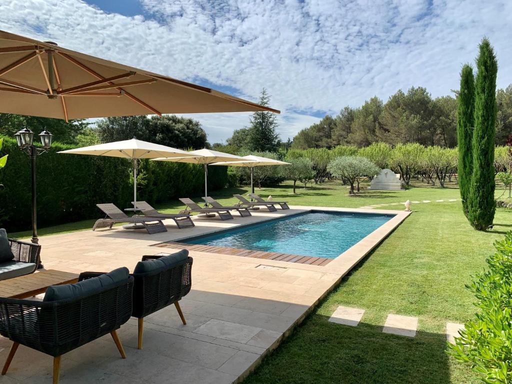 a pool with chairs and umbrellas in a yard at Le Jardin des Amandiers in Châteaurenard