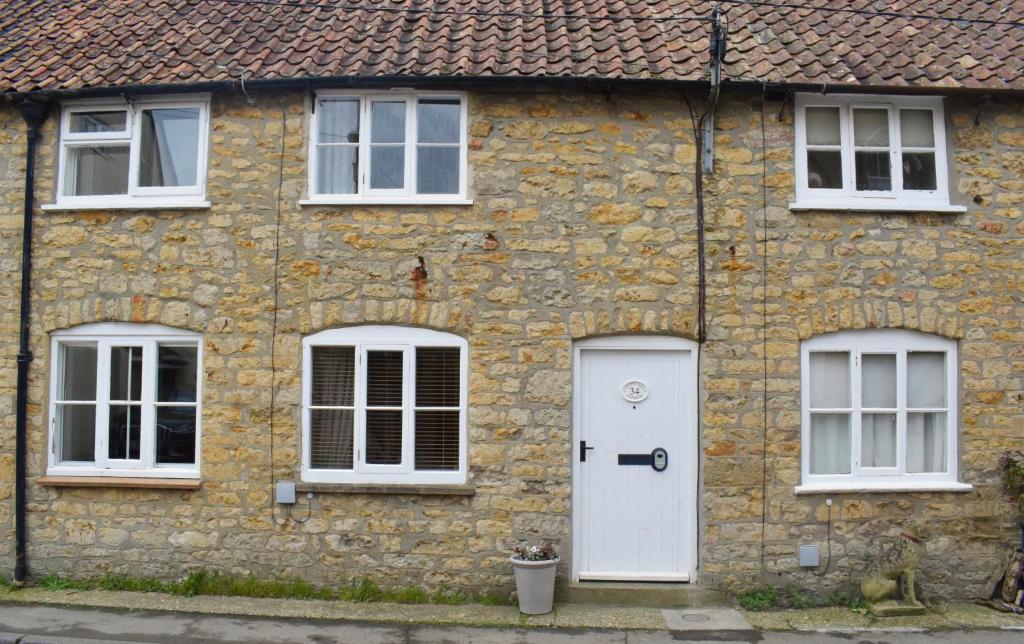 a stone house with a white door and three windows at Chapel View Cottage in Beaminster