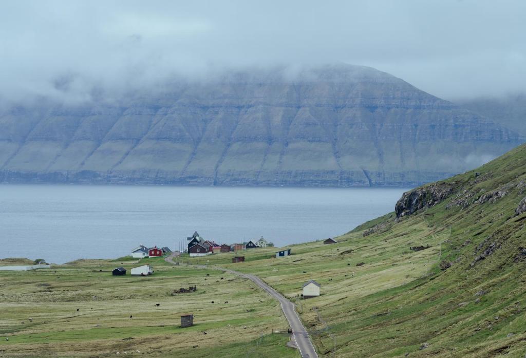 ein Grashügel mit einem Bauernhof und einem Wasserkörper in der Unterkunft Authentic Faroese House / Unique Location / Nature in Hellur