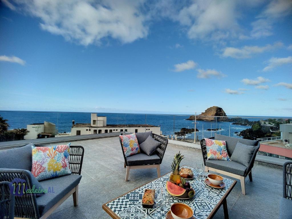 un patio con mesa, sillas y el océano en Pearls Beach Penthouse, en Porto Moniz