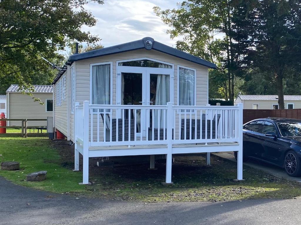 a small white house with a porch and a car at Prestige Static Caravan on 5 Star Holiday Park in Cheswick