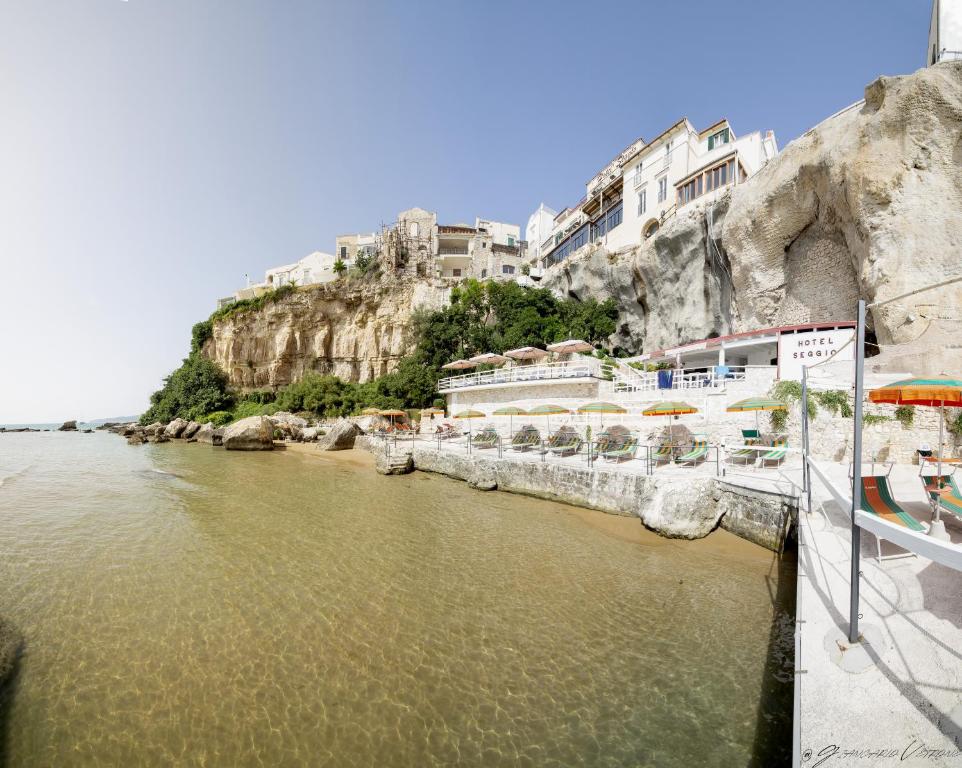a river with umbrellas and buildings on a cliff at Hotel Seggio in Vieste