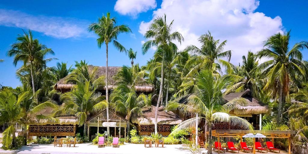The Coral Blue Oriental Beach Villas and Suites في جزيرة بانتايان: منتجع فيه نخيل وطاولات وكراسي
