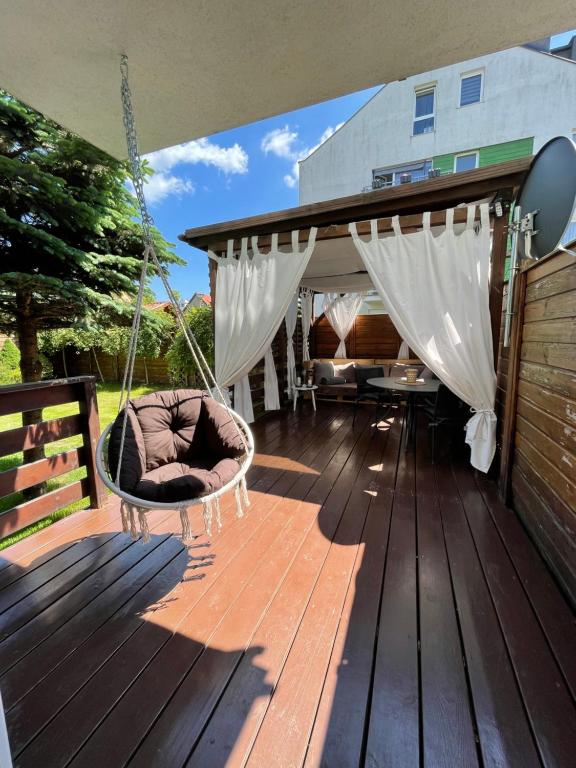 une terrasse couverte avec une balançoire sur une terrasse en bois dans l'établissement Ogród Victorii - Apartament z dużym ogrodem, tarasem i altaną, à Gdańsk