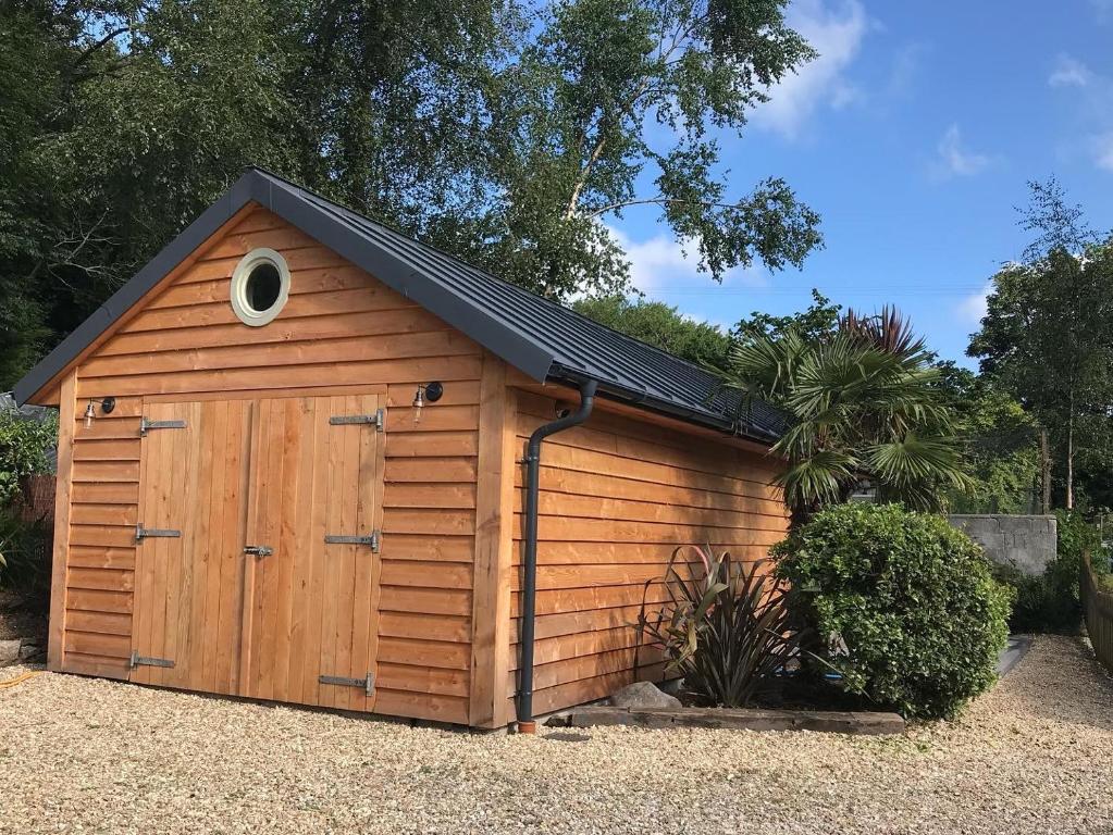 een houten garage met een zwart dak bij The Potting Shed in St Austell