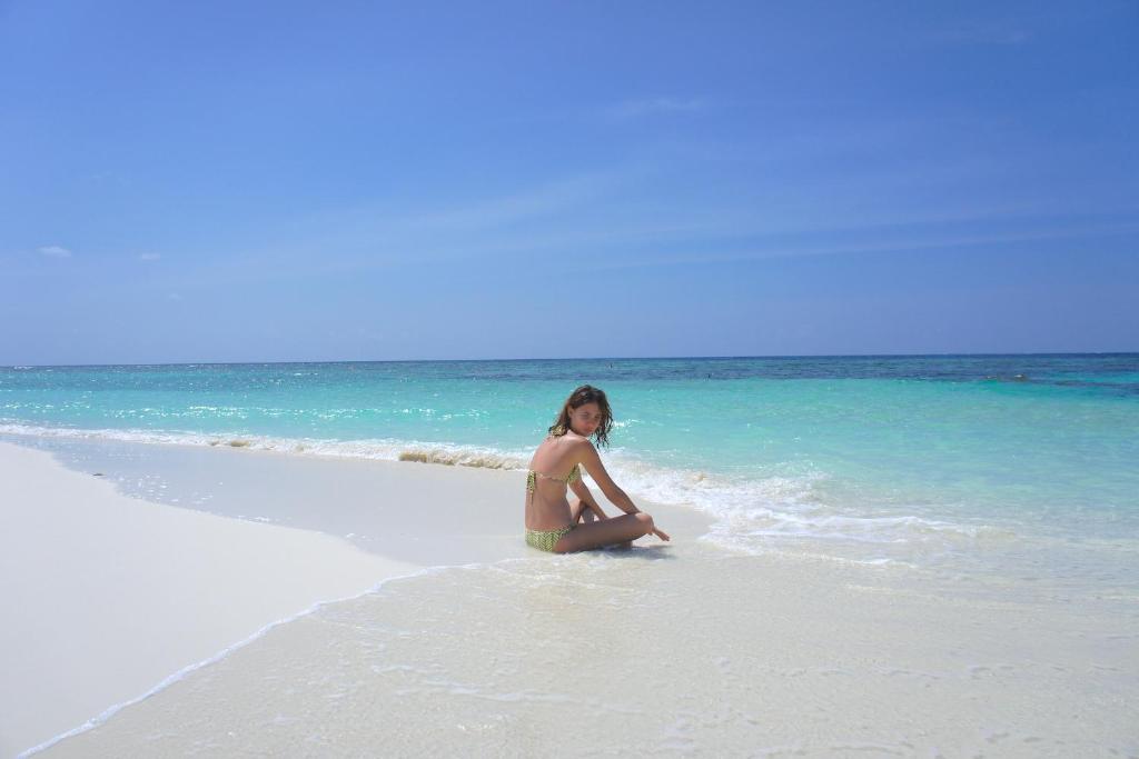 a woman sitting in the water on a beach at Kaani Beach Hotel in Maafushi