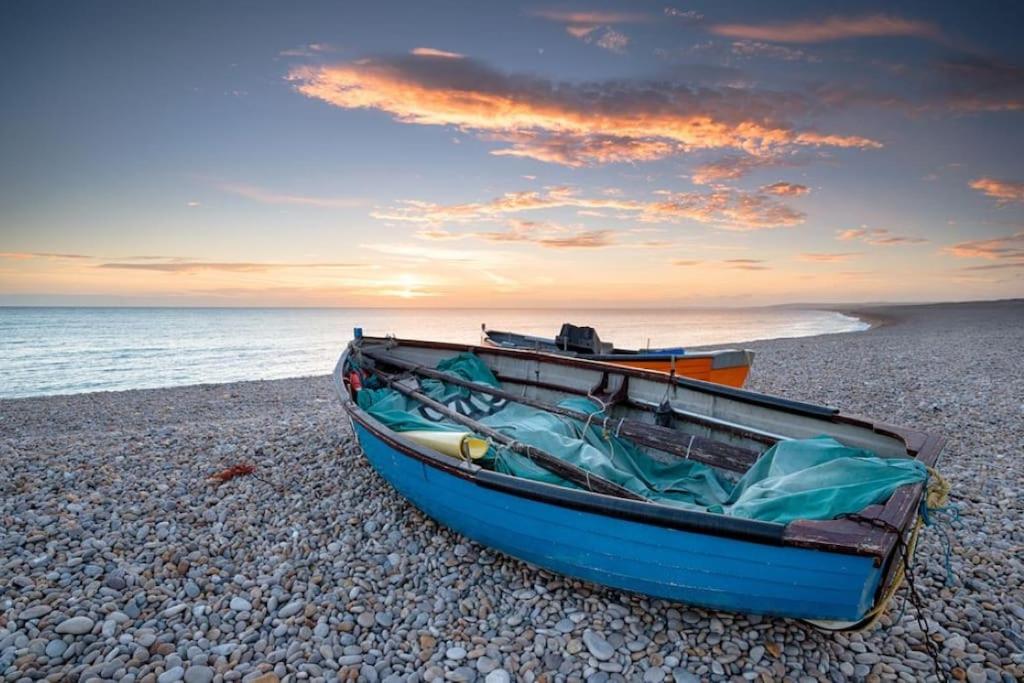 a blue boat sitting on a rocky beach at Luxurious Beach House Chesil Beach. Sleeps 6 in Castletown