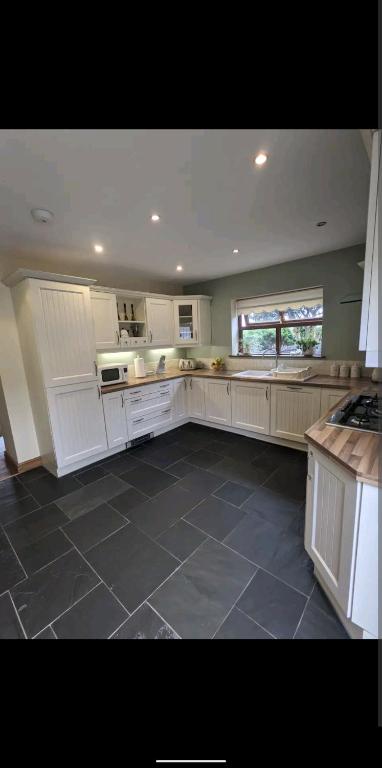 una grande cucina con armadi bianchi e pavimento piastrellato di Sunset cottage a Burry Port