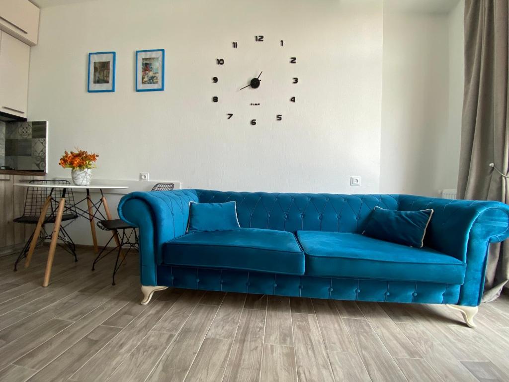 Sofá azul en la sala de estar con reloj en la pared en Studio apartment with balcony in Tbilisi en Tiflis