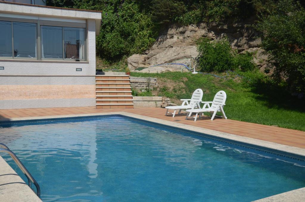 a swimming pool with two chairs and a house at Hotel Palacios in Sanxenxo