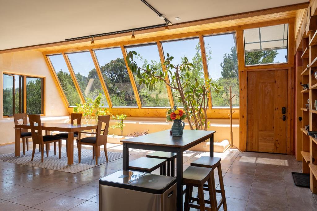 a dining room with a table and chairs and windows at Earthship retreat + 2 spas + incredible views. in Santa Fe