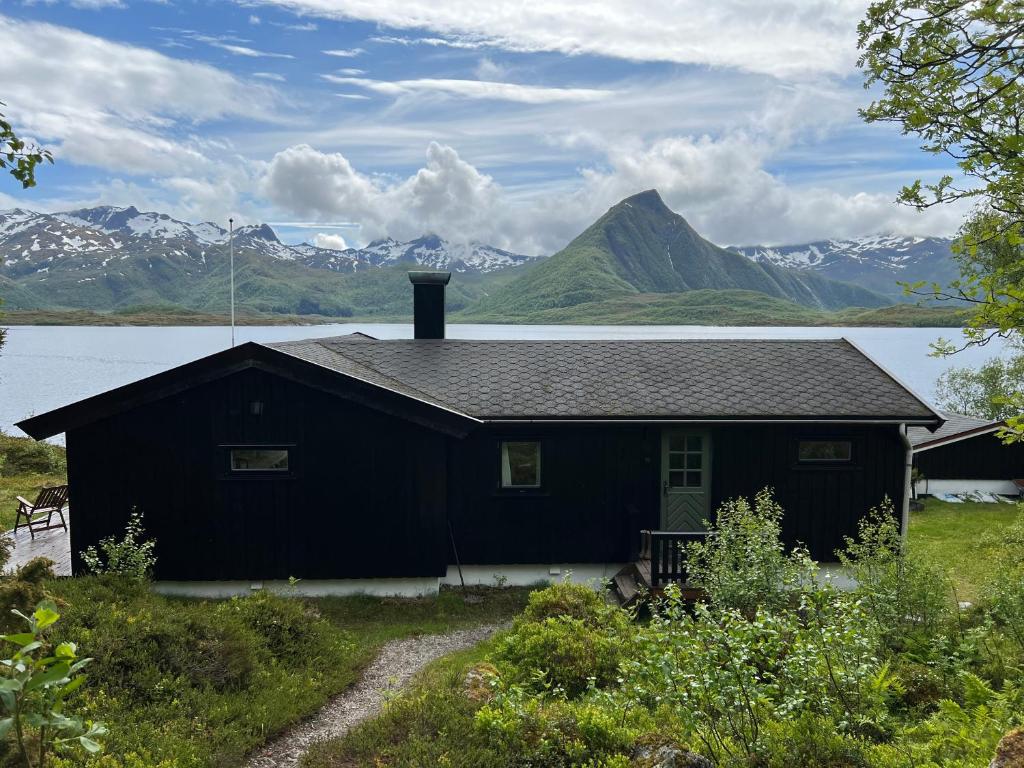 a black house with mountains in the background at Cosy and authentic cabin in Lofoten in Sandsletta